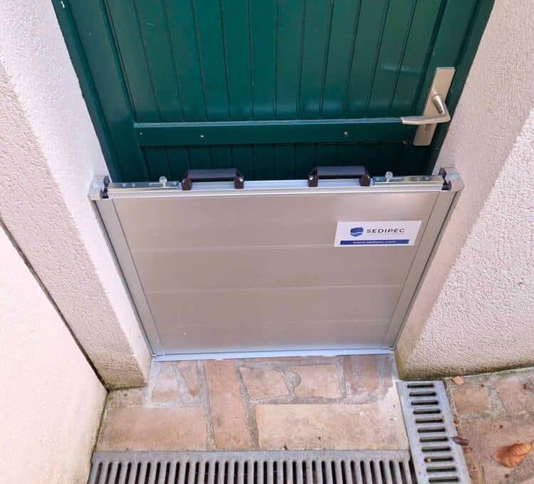 Barrière anti-inondation en aluminium installée devant une porte d'entrée de maison